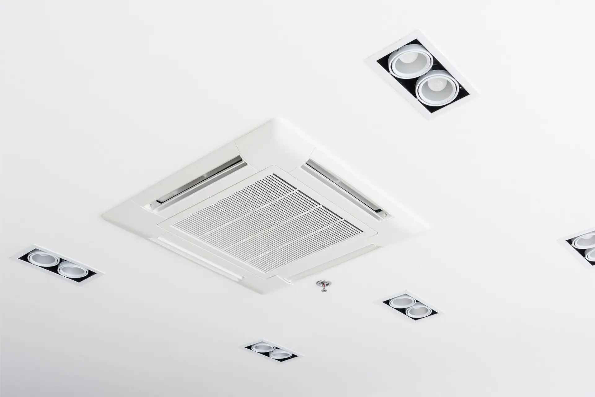 Ceiling-mounted cassette air conditioning unit installed in a white ceiling with downlights